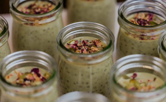 Glass jars filled with creamy chia pudding topped with dried rose petals and seeds, arranged in rows.