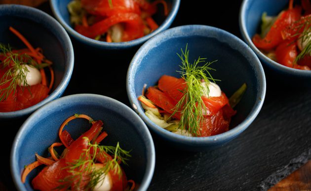 Small blue bowls filled with smoked salmon, thinly sliced vegetables, and a dollop of crème fraîche, garnished with fresh dill.